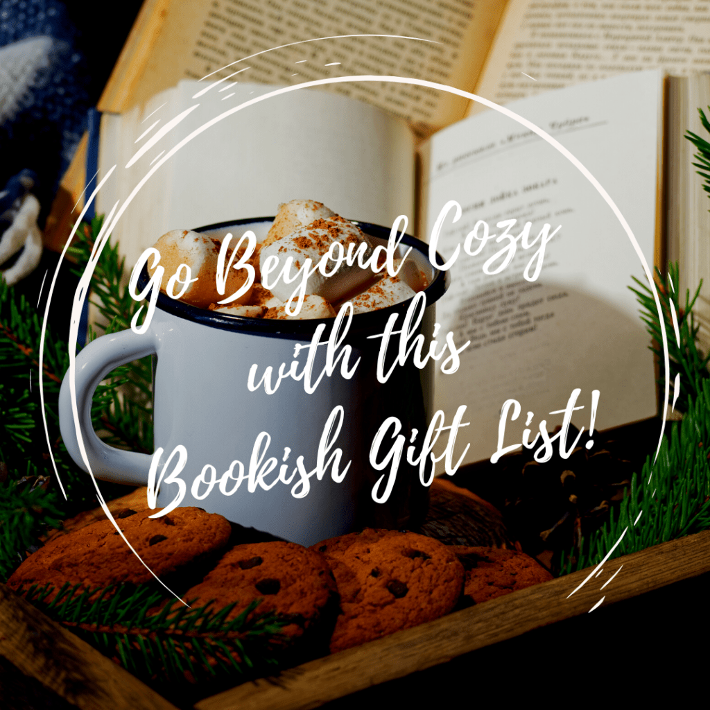 A mug of hot cocoa and a plate of cookies sits in front of an open book surrounded by evergreen boughs.